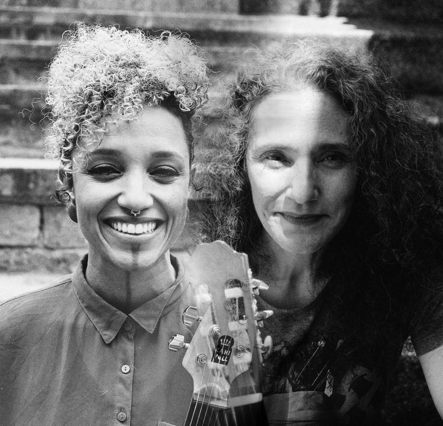 Das Bild zeigt Das Duo Badi Assad und Anna Trea in schwarz-weiß. Es ist ein Selfie vor einer Steintreppe. Sie lächeln beide freundlich in die Kamera. Zwischen ihnen sieht man die Köpfe zweier Gitarren. Das Gesicht von Badi Assad ist zur Hälfte im Schatten