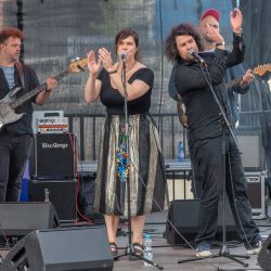 Das Bild zeigt 4 Musiker auf der Bühne. Im Vordergrund 2 Sänger, welche jeweils in eine andere Richtung gedreht sind und ihre Hände heben um zu klatschen. Im Hintergrund stehen zwei Gitarristen.