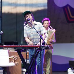 Ein Mann steht am Keyboard, dieser singt zusätzlich noch. Im Hintergrund steht ein Mann im grünen Anzug mit Saxophon  in der Hand.